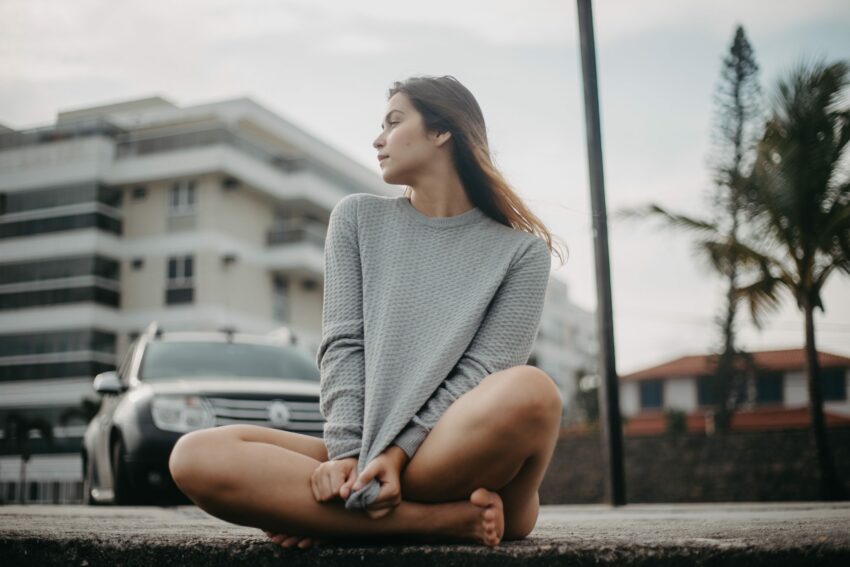 woman in gray sweater sitting on brown concrete floor during daytime